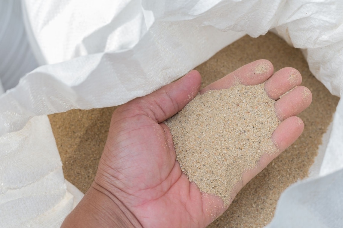 Hand greift in Sack voller Bausand