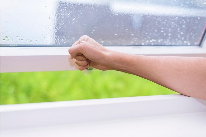 Hand schließt Fenster bei Regen