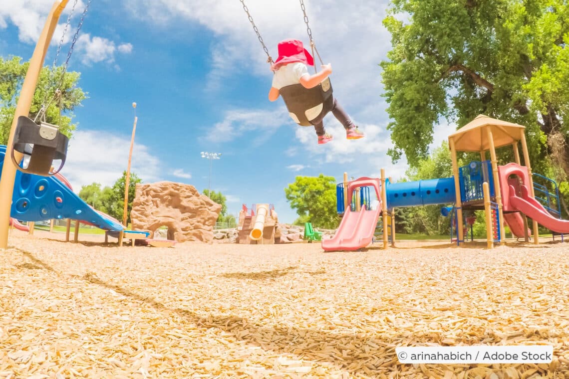 Kind schaukelt auf Spielplatz, Holzhäcksel als Fallschutz