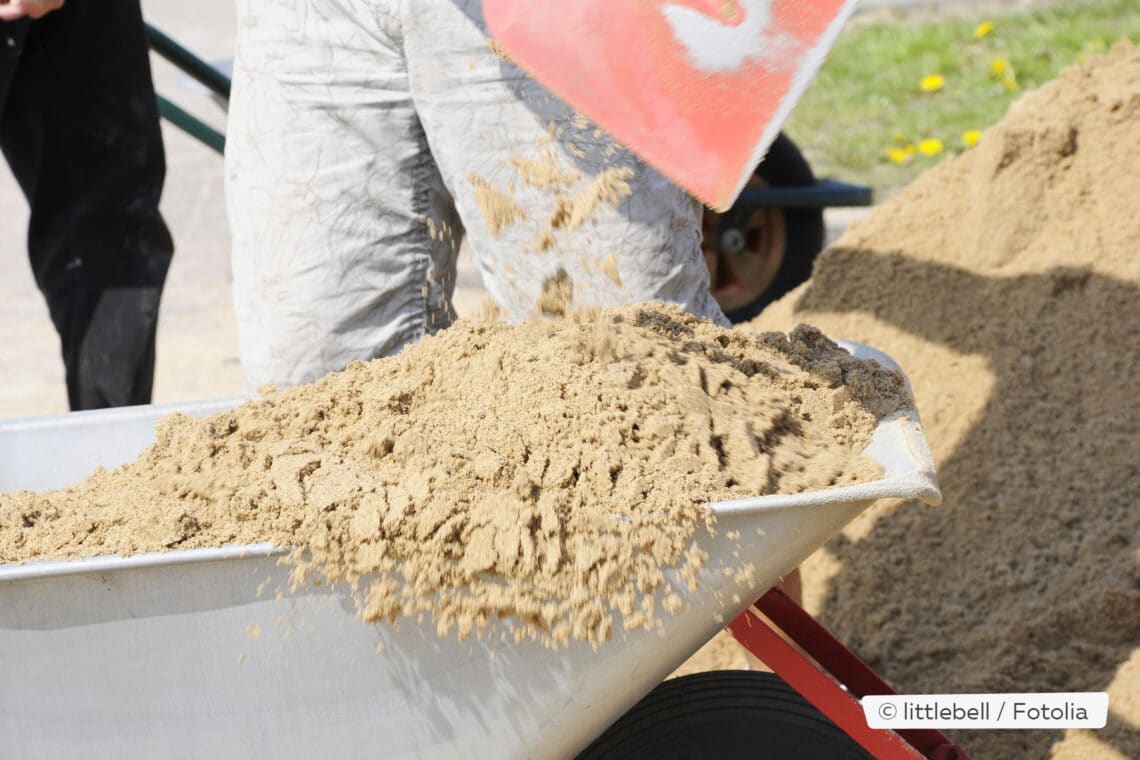 Sand mit Schaufel in Schubkarre schippen