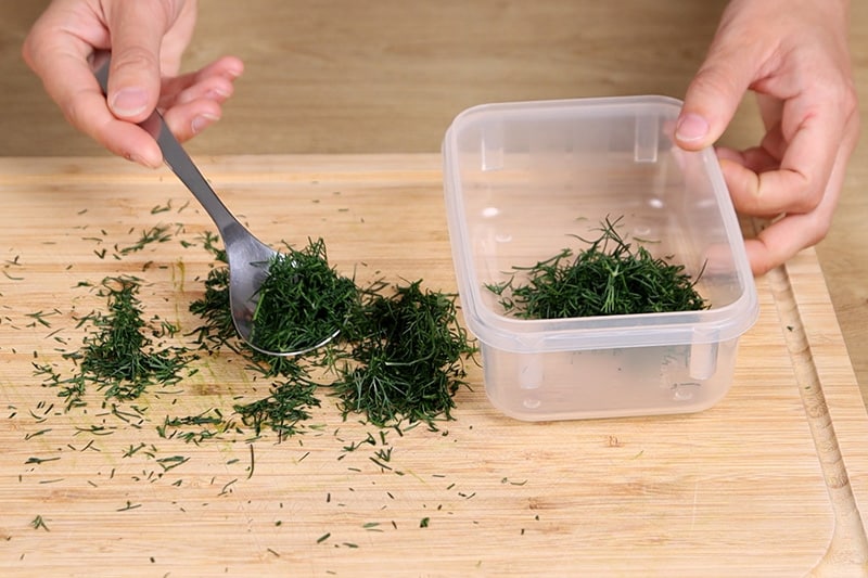 Dill in Plastedose mit Löffel geben