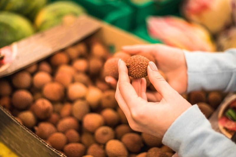 Hände prüfen Litschis im Supermarkt auf Reife