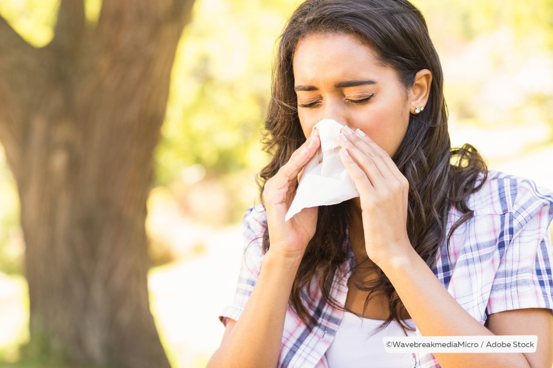 Allergiesymptome, Frau niest vor Baum in der Natur